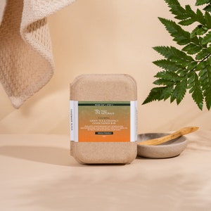 May include: A brown cardboard box containing a green tea and coconut conditioner bar. The bar is labeled "Calming" and "Tree Naturals". The box is handmade in RVA and is vegan friendly.