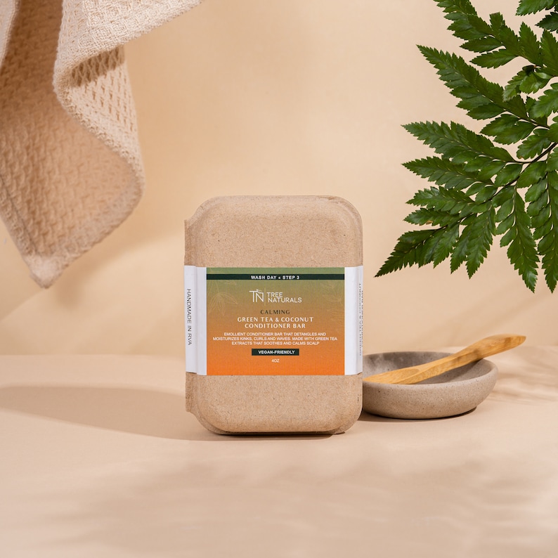 May include: A brown cardboard box containing a green tea and coconut conditioner bar. The bar is labeled "Calming" and "Tree Naturals". The box is handmade in RVA and is vegan friendly.