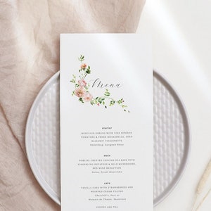 Może przedstawiać: Biała karta menu z kwiatowym wzorem w lewym górnym rogu. Menu zawiera przystawkę, danie główne i deser. Tekst brzmi: "Menu", "Przystawka", "Mesculin Greens with Five Ripened Tomatoes & Burrata, Basil & Pesto, Parmesan Shavings, Aged Balsamic Vinaigrette", "Danie główne", "Porcini Crusted Chilean Sea Bass with Fingerling Potatoes & Wild Mushrooms, Red Wine Reduction", "Deser", "Vanilla Cake with Strawberries and Whipped Cream Filling, Chocolate, Fruit or Marquise de Chocolat,  Satiens", "Kawa i herbata".