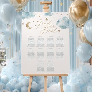 May include: A wedding seating chart on an easel, with a celestial theme. The sign features a gold script that reads "find your seat" with watercolor clouds, a crescent moon, and stars. Balloons in gold and light blue surround the sign.