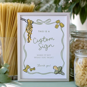 May include: A framed custom sign with a silver border, featuring pasta-themed illustrations and the text "THIS IS A Custom Sign MAKE IT SAY WHAT YOU WANT Thank you!". The sign is on a light green surface, with pasta and flowers in the background.