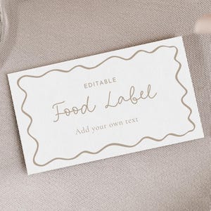 Könnte beinhalten: Ein weißes rechteckiges Lebensmitteletikett mit einem wellenförmigen braunen Rand. Auf dem Etikett steht "EDITABLE Food Label Add your own text" in einer handschriftlichen Schriftart. Das Etikett liegt auf einem hellgrauen Stoff.