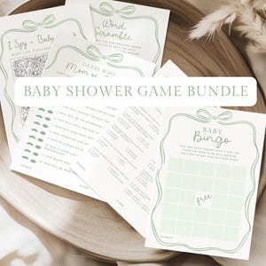 May include: A collection of baby shower game cards in a wooden tray. The cards feature green accents and include games like "I Spy," "Word Scramble," and "Baby Bingo." The text "Baby Shower Game Bundle" is visible.