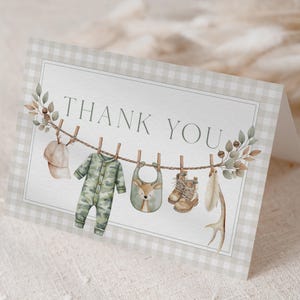 Może przedstawiać: Złożona kartka z podziękowaniami na baby shower z obramowaniem w kratkę. Karta przedstawia sznur do wieszania ubranek dla dzieci, w tym kombinezon w kamuflażu, śliniaczek i buty. Słowa "THANK YOU" są wydrukowane na zielono.