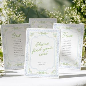 May include: A set of white rectangular wedding seating chart cards with blue scalloped borders and green floral accents. The central card reads "Please find your seat" with "Emily & David May 14, 20xx" below. Other cards display table numbers and guest names.