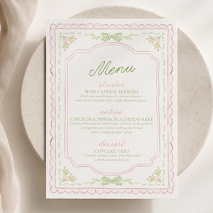 May include: A rectangular menu card featuring a scalloped pink border with delicate green floral accents. The text reads Menu, starter, MINI CAPRESE SKEWERS, entrée, CHICKEN & SPINACH ALFREDO BAKE, dessert, and CUPCAKE TRIO with detailed descriptions.