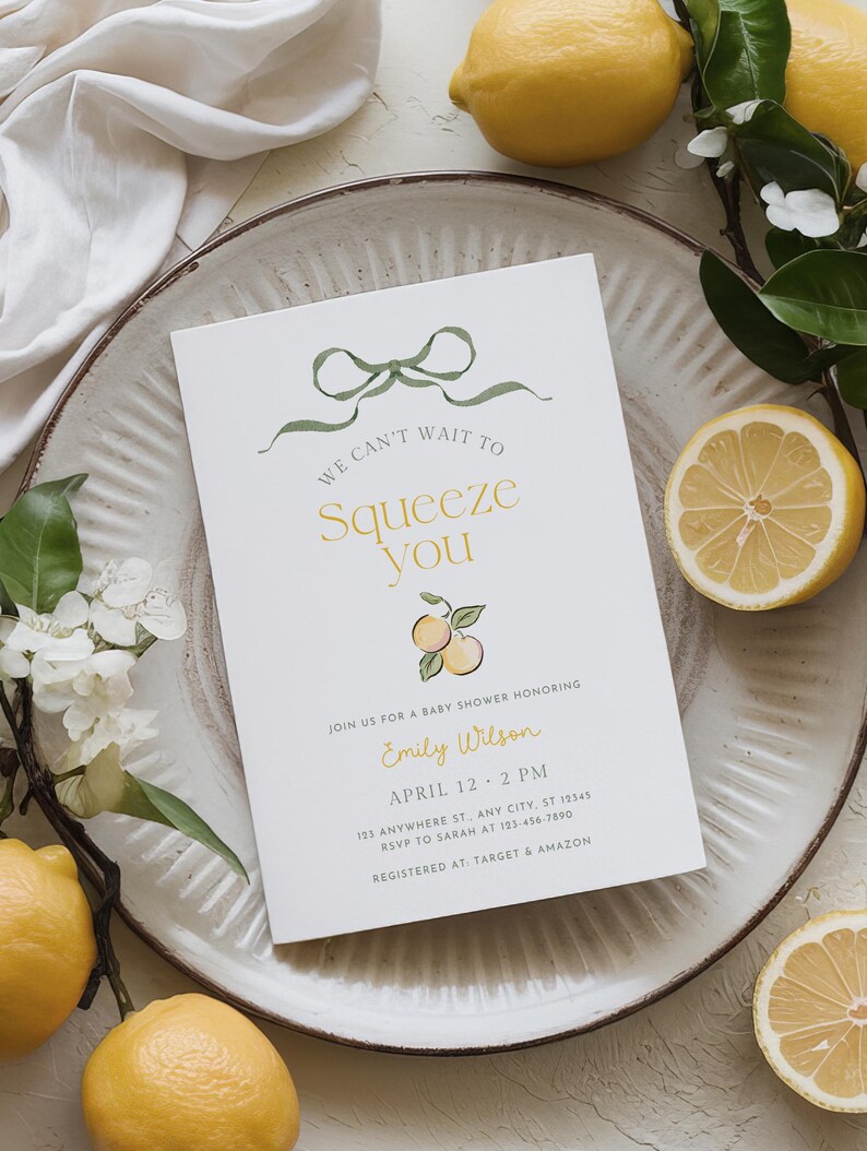 May include: A baby shower invitation with the text "We can't wait to squeeze you" in gold and green. The invitation features a lemon theme with illustrations and real lemons. The invitation is on a white background.