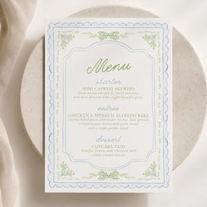 Peut inclure: Une carte de menu rectangulaire avec une bordure festonnée bleu clair et des motifs floraux verts. Le texte indique Menu, starter, MINI CAPRESE SKEWERS, entrée, CHICKEN & SPINACH ALFREDO BAKE, dessert, et CUPCAKE TRIO, avec des descriptions.