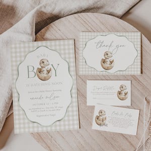 May include: A baby shower invitation set with a dinosaur theme. The main invitation features a baby dinosaur hatching from an egg, with the text "Baby Boy is Hatching Soon." Additional cards include a thank you, diaper raffle, and books for baby.
