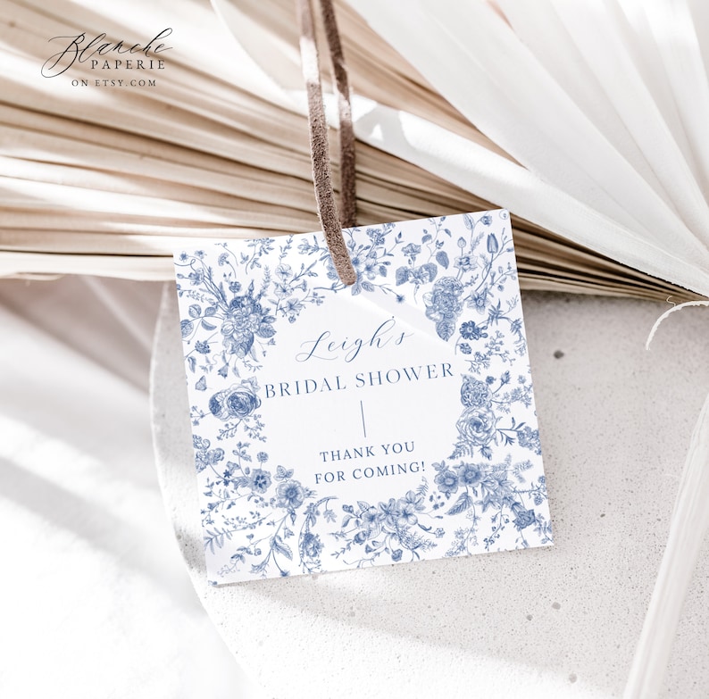 May include: A white bridal shower favor tag with a blue floral pattern. The tag says "Leigh's Bridal Shower" and "Thank You For Coming!"