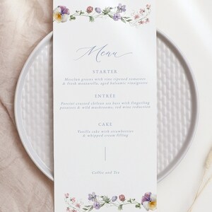 May include: A wedding menu with a floral border. The menu lists the starter, entree, cake, and coffee and tea. The starter is mesclun greens with vine ripened tomatoes and fresh mozzarella, aged balsamic vinaigrette. The entree is porcini crusted chilean sea bass with fingerling potatoes and wild mushrooms, red wine reduction. The cake is vanilla cake with strawberries and whipped cream filling.