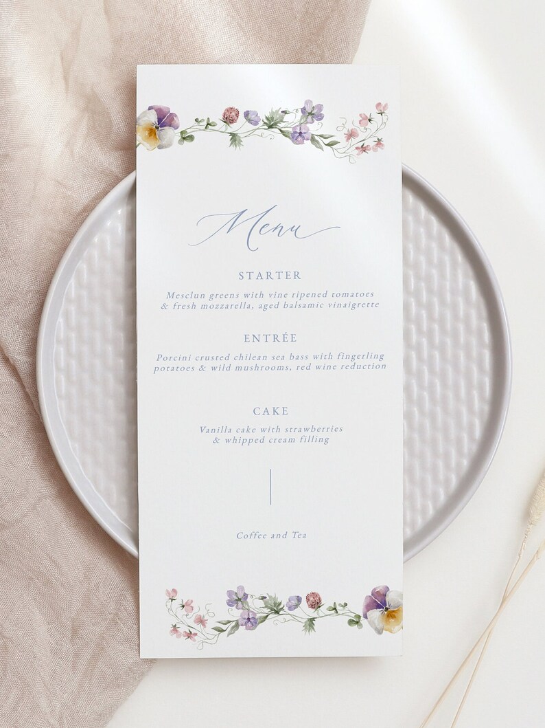May include: A wedding menu with a floral border. The menu lists the starter, entree, cake, and coffee and tea. The starter is mesclun greens with vine ripened tomatoes and fresh mozzarella, aged balsamic vinaigrette. The entree is porcini crusted chilean sea bass with fingerling potatoes and wild mushrooms, red wine reduction. The cake is vanilla cake with strawberries and whipped cream filling.