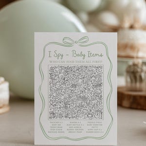May include: A baby shower game card with the text "I Spy - Baby Items". The card features a detailed black and white illustration of baby-related objects. The card includes a list of items to find, such as pacifiers, diapers, and a rocking horse.
