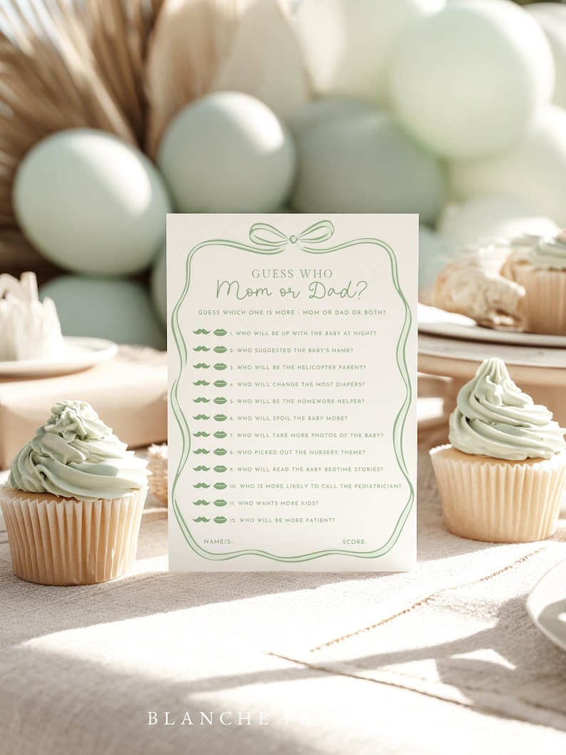 May include: A baby shower game card with the text "Guess Who Mom or Dad?" in a green frame, with questions about the parents. Two cupcakes with green frosting are in the foreground, with balloons in the background.