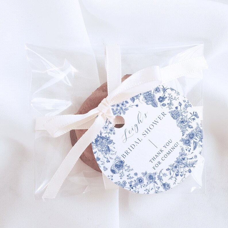 May include: A white round tag with blue floral designs and the text "Leigh's Bridal Shower" and "Thank you for coming!"