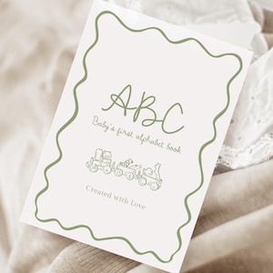 May include: A baby's first alphabet book with a green wavy border. The cover features the letters "ABC" in a handwritten style, with the text "Baby's first alphabet book" below. A train illustration is at the bottom, with the words "Created with Love".
