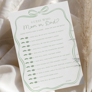 May include: A white card with a green border and text that reads "Guess Who Mom or Dad?" with questions about parenting. The card has a bow design at the top and mustache and lips icons.