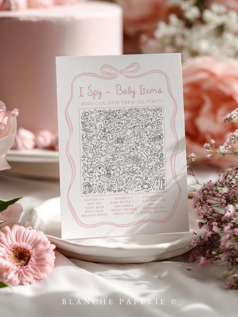 Pu&ograve; includere: Una carta bianca con dettagli rosa, con il testo "I Spy - Baby Items" e un'illustrazione dettagliata in bianco e nero di oggetti per bambini. La carta &egrave; su un piatto bianco, circondata da fiori rosa.