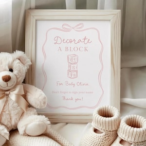 Pu&ograve; includere: Un cartello incorniciato con la scritta "Decorate A Block" in rosa, con un orsacchiotto, una coperta di lana e due paia di scarpine per neonati. Il cartello &egrave; per Baby Olivia e include una richiesta di firmare il tuo nome.