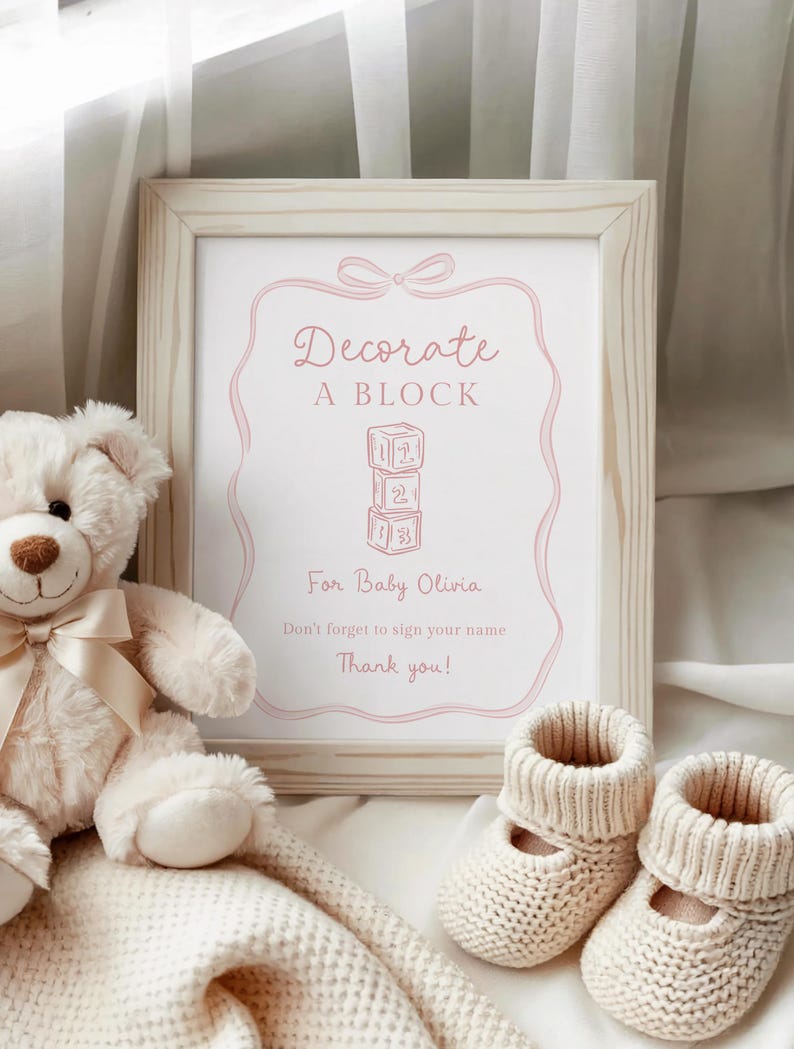 Pu&ograve; includere: Un cartello incorniciato con la scritta "Decorate A Block" in rosa, con un orsacchiotto, una coperta di lana e due paia di scarpine per neonati. Il cartello &egrave; per Baby Olivia e include una richiesta di firmare il tuo nome.