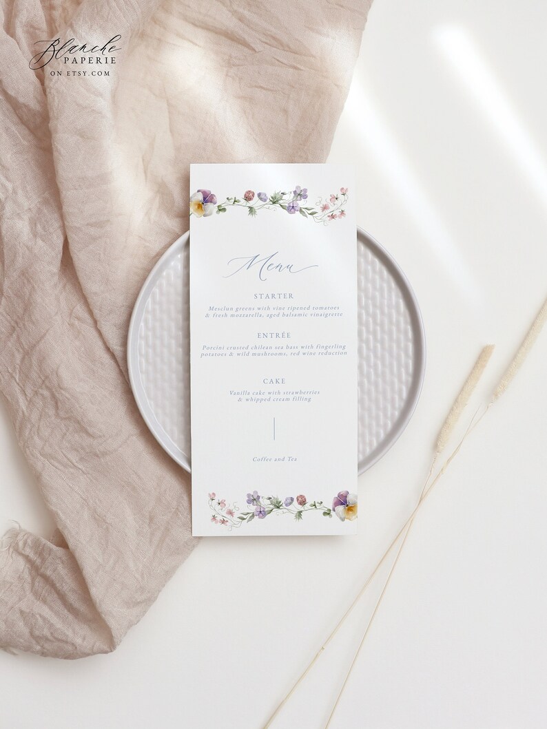 May include: A wedding menu card with a floral border. The menu includes a starter, entree, cake, and coffee and tea. The text is in a light blue font.