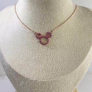 May include: A rose gold necklace featuring a pendant in the shape of a mouse head. The pendant is made of small, round, pink gemstones. The necklace is displayed on a mannequin.