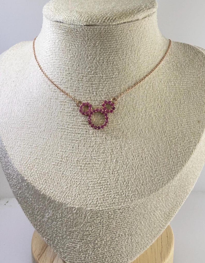 May include: A rose gold necklace featuring a pendant in the shape of a mouse head. The pendant is made of small, round, pink gemstones. The necklace is displayed on a mannequin.