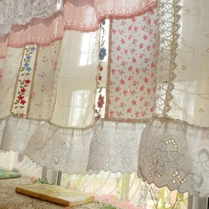 May include: A white sheer curtain with a lace trim and patchwork design. The curtain is made of different fabrics with floral patterns and embroidery. The curtain is hung on a window with sunlight shining through.