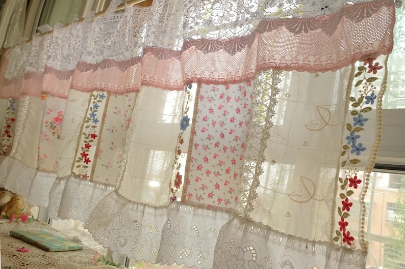 May include: A white and pink patchwork curtain with lace trim and floral embroidery. The curtain is made of different fabrics and has a vintage look.