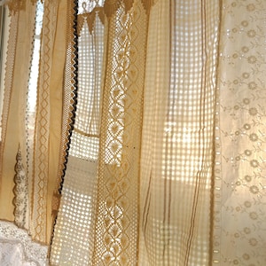 Puede incluir: Cortinas de encaje de estilo vintage en varios tonos crema y beige. Las cortinas presentan patrones intrincados, incluyendo bordados florales, diseños geométricos y bordes festoneados. La luz del sol se filtra a través de la tela, creando un brillo suave y cálido.