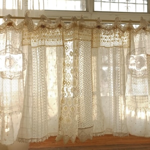 May include: Cream lace curtains hanging in front of a window. The curtains are made of various lace patterns, creating a patchwork effect. Sunlight filters through the delicate fabric, illuminating the room. The curtains are a vintage style.