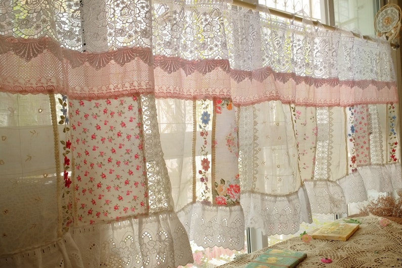 May include: A white and pink patchwork curtain with lace trim. The curtain is made of different fabrics, including lace, floral print, and plain white. The curtain is hung on a window with a wooden rod.