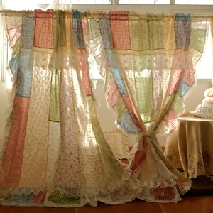 Puede incluir: Cortinas de patchwork con una mezcla de paneles de tela floral, cuadros y lisos en colores pastel. Las cortinas están adornadas con encaje y atadas en el centro, creando un aspecto suave y romántico. Las cortinas cuelgan frente a una ventana.