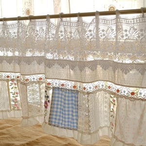May include: Cream-colored lace curtains with floral and scalloped trim. The curtains are hung on a wooden rod and feature various fabric panels, including a blue and white checkered pattern. The design is vintage and cottagecore.