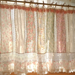 May include: A set of floral patterned curtains in pink, white, and green hang from a wooden rod. The curtains have lace trim and a scalloped edge, creating a romantic, vintage look. The top of the curtains are decorated with pink rosettes.