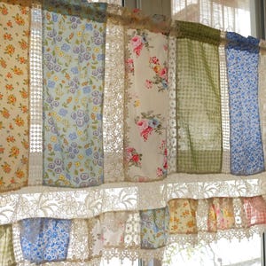 Può includere: Una tenda a valance in patchwork con un mix di motivi floreali e gingham in tonalità di blu, verde e giallo. La valance è rifinita con pizzo bianco e ha un fondo arricciato.