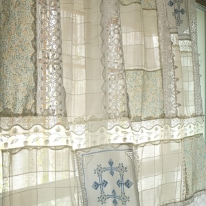 Peut inclure: Rideaux patchwork crème avec des motifs floraux et quadrillés. Les rideaux présentent des bordures en dentelle et des carrés brodés avec des motifs de croix bleues. Le design est un mélange de textures et de motifs, créant une esthétique vintage et artisanale.