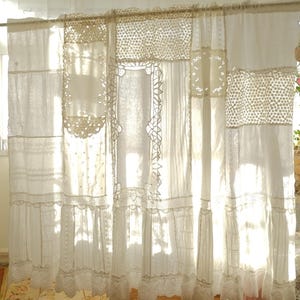 Peut inclure: Panneaux de rideaux blancs en dentelle et lin. Les panneaux sont faits de divers tissus blancs, dont de la dentelle et du lin, et sont cousus ensemble dans un style patchwork. Les rideaux sont suspendus à une tringle et la lumière du soleil les traverse.
