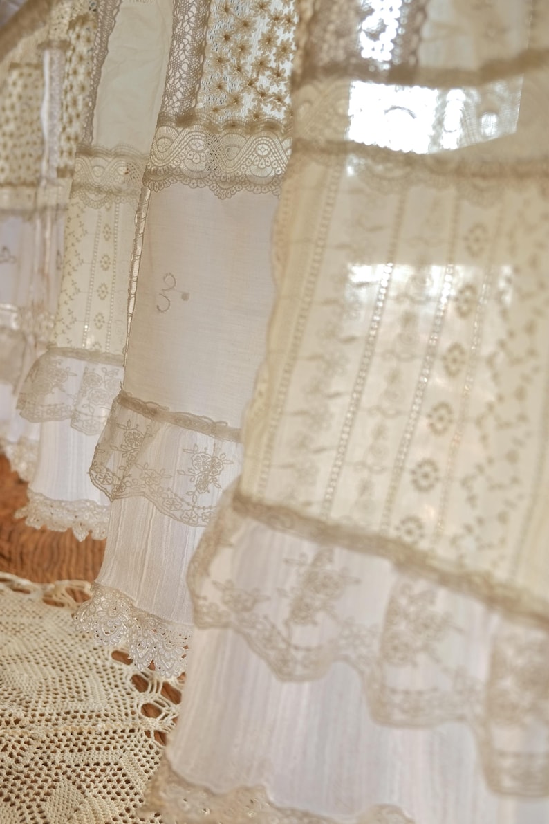 Puede incluir: Cortinas de encaje blanco con un delicado patr&oacute;n floral. Las cortinas est&aacute;n superpuestas y tienen un borde con volantes.