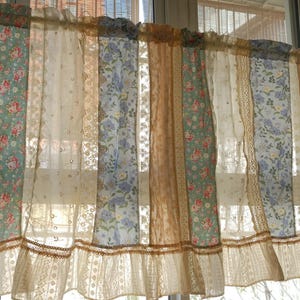 May include: A patchwork curtain featuring a combination of floral and lace designs in beige, blue and green hues. The curtain has a frilled bottom edge.