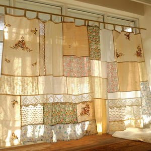 May include: A patchwork curtain made from a variety of fabrics, including floral prints, lace, and embroidered details. The curtain hangs from a wooden rod, with a mix of beige, cream, and floral patterns. A decorative window treatment.
