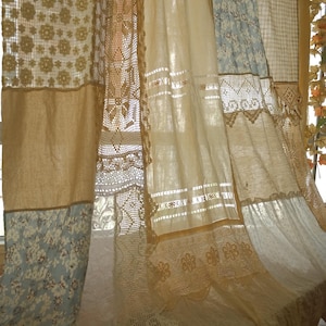 Pode incluir: Uma cortina de patchwork com uma mistura de tecidos, incluindo estampas florais, serapilheira e renda. A cortina apresenta tons bege, creme e azul claro. O design incorpora diferentes texturas e padrões, criando uma estética vintage ou boêmia.