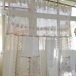 May include: White lace curtains with intricate crochet and embroidered details. The curtains hang from a wooden rod, creating a delicate and airy window treatment. The design features various patterns and textures.