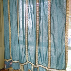 May include: A blue curtain panel featuring vertical strips of beige lace trim. The lower section of the curtain is accented with a horizontal band of lace and alternating patches of blue fabric with floral patterns and solid blue fabric panels.
