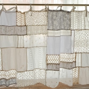 Puede incluir: Panel de cortina patchwork con una variedad de telas blancas y beige. La cortina presenta cuadrados de encaje, materiales punteados y a rayas. La parte superior tiene cierres de lazo y cuelga de una barra dorada. El diseño general es una mezcla de texturas y patrones.