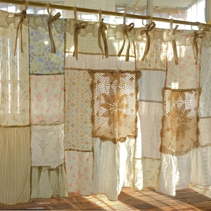 Può includere: Una tenda patchwork con vari tessuti floreali e fantasia in morbidi colori pastello. La tenda presenta pannelli all'uncinetto ed è sospesa a un'asta di legno con fiocchi di nastro, creando un'estetica vintage e cottagecore.