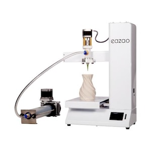 Peut inclure: Une imprimante 3D Eazao blanche avec une tour verticale, une tête d'impression avec buse et un plateau plat. Un tube transparent relie la tête à un extrudeur cylindrique séparé. Un vase en céramique blanc en spirale est sur le plateau.