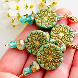 May include: Four teal blue and gold patterned round beads with gold accents and clear glass beads on a gold chain. The beads are strung on a gold chain with a gold clasp.