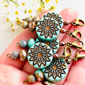 May include: Set of four turquoise blue and brown patterned stitch markers with gold metal clasps and brown and white beads.