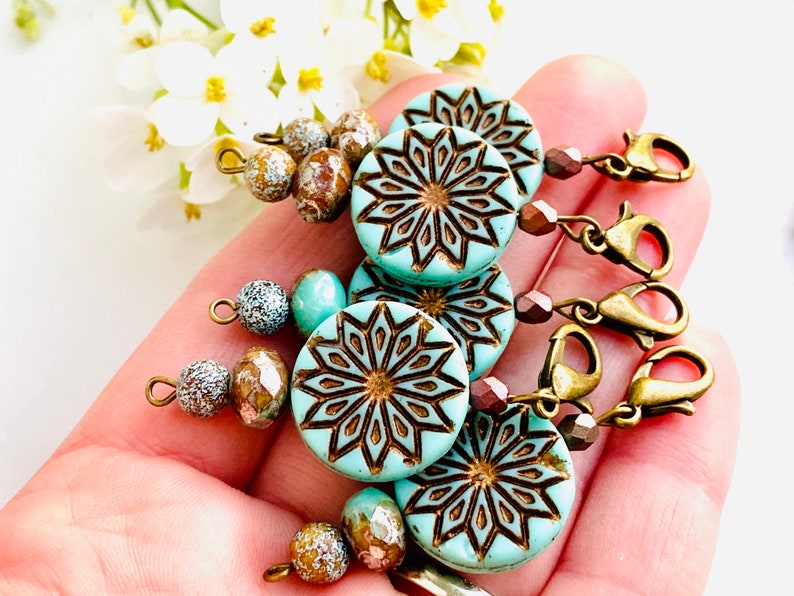 May include: Set of four turquoise blue and brown patterned stitch markers with gold metal clasps and brown and white beads.